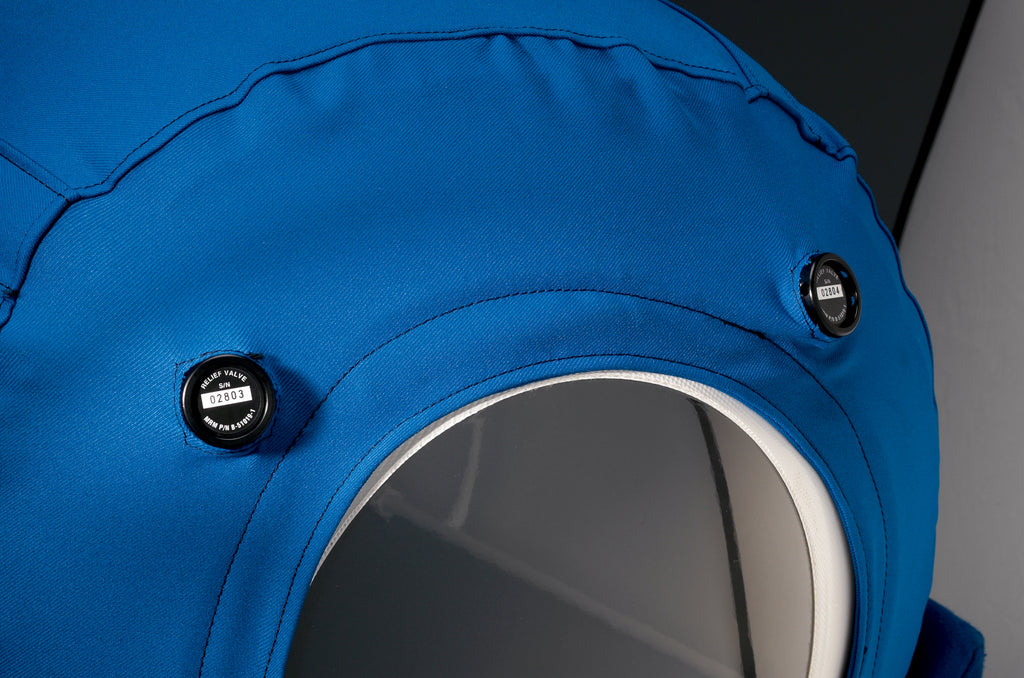 A blue inflatable hyperbaric chamber with clear viewing windows along the top side and a front circular port.